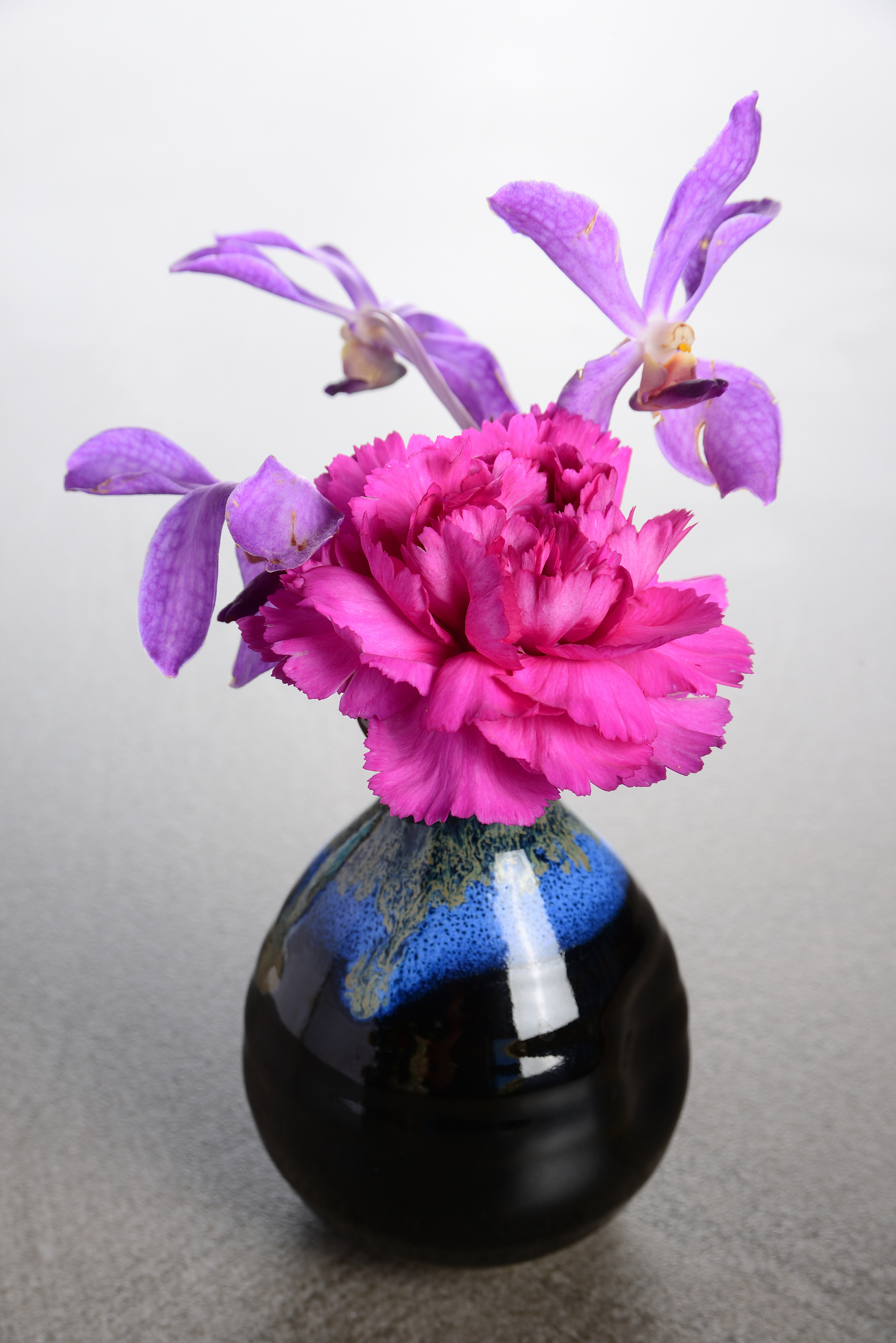 黒に藍の釉薬の花瓶 あざやかなピンクのカーネーションと紫の蘭